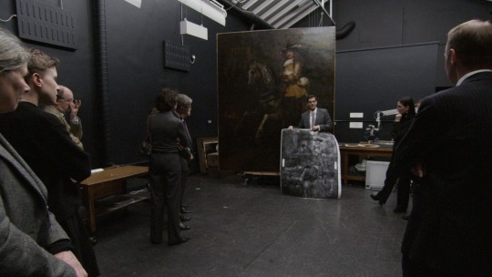 Film still. Visitors are shown Rembrandt's Portrait of Frederick Rihel on Horseback, and the x-ray image of the painting